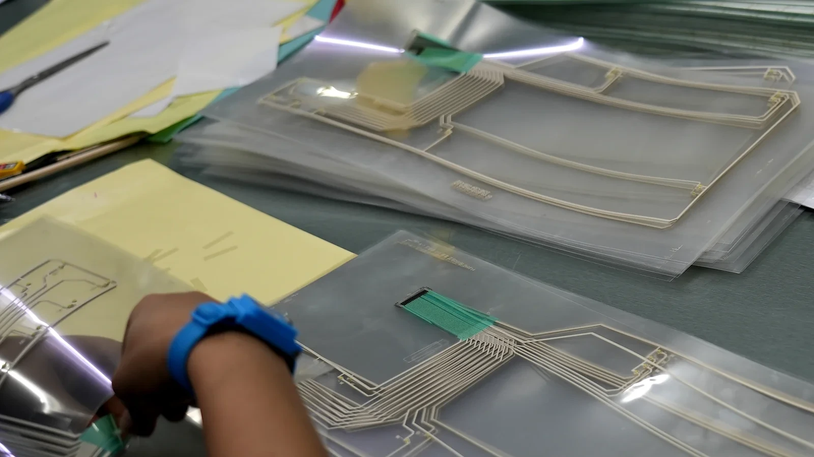 Operator aligning a silver-printed PET circuit layer during membrane switch assembly